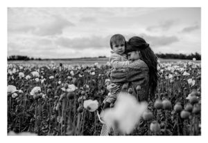 Black and white portrait of mother and child in a field of white poppies under cloudy skies.