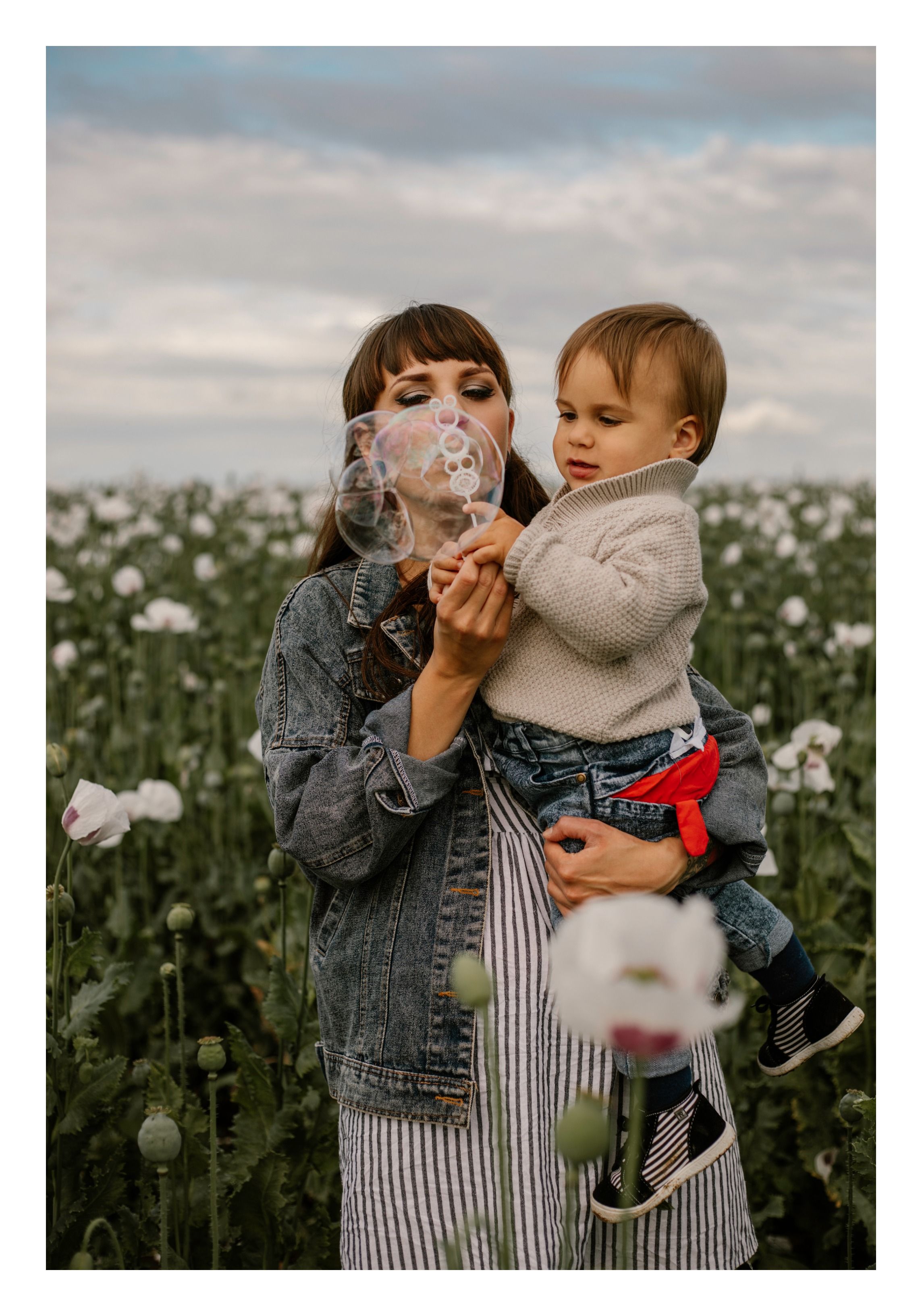 Mother and child playing with poppy seeds in flowering field during sunset.