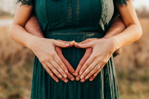 Hands form a heart shape over an emerald green dress in a rustic outdoor setting.
