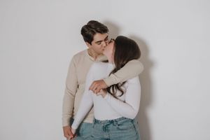 A couple in neutral sweaters share a tender romantic moment against a white wall.