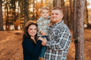 A loving family portrait captured in a forest setting with warm autumn colors and fallen leaves.