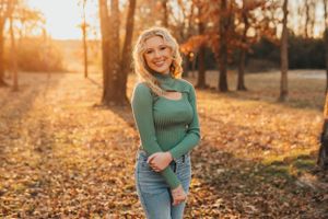 Teen in green sweater poses in autumn setting with golden sunlight.