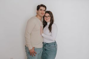A couple in casual attire poses intimately against a minimalist white backdrop.