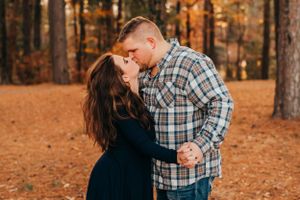 A romantic couple embraces in a wooded area during golden hour with fallen autumn leaves.