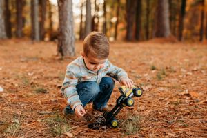 Young child plays with toy truck on ground covered in pine needles during autumn.