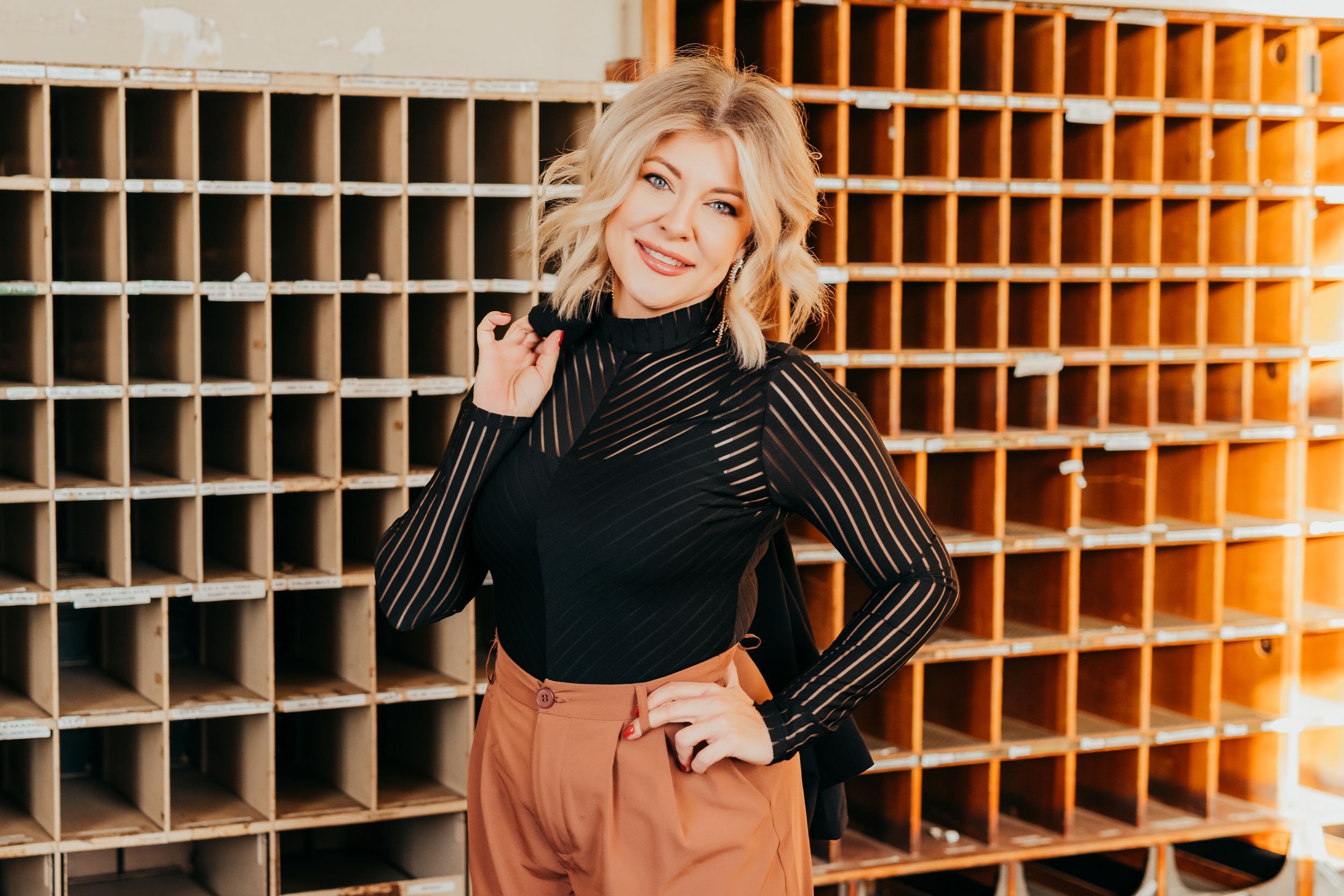 Stylish headshot in black turtleneck and tan pants against wooden storage wall.