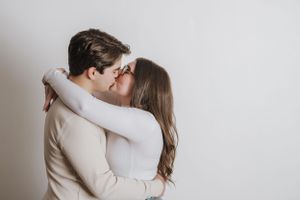 Intimate moment between couple in neutral colored clothing against white backdrop.