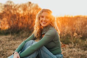 Teen sitting outdoors in green sweater during sunset with golden light.