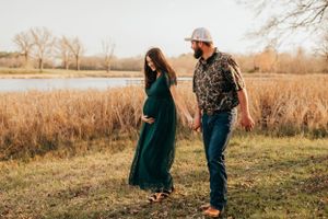 A couple holds hands while walking through golden autumn grass near a lake.