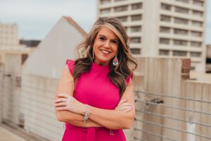 Woman in bright pink dress poses confidently on urban rooftop.