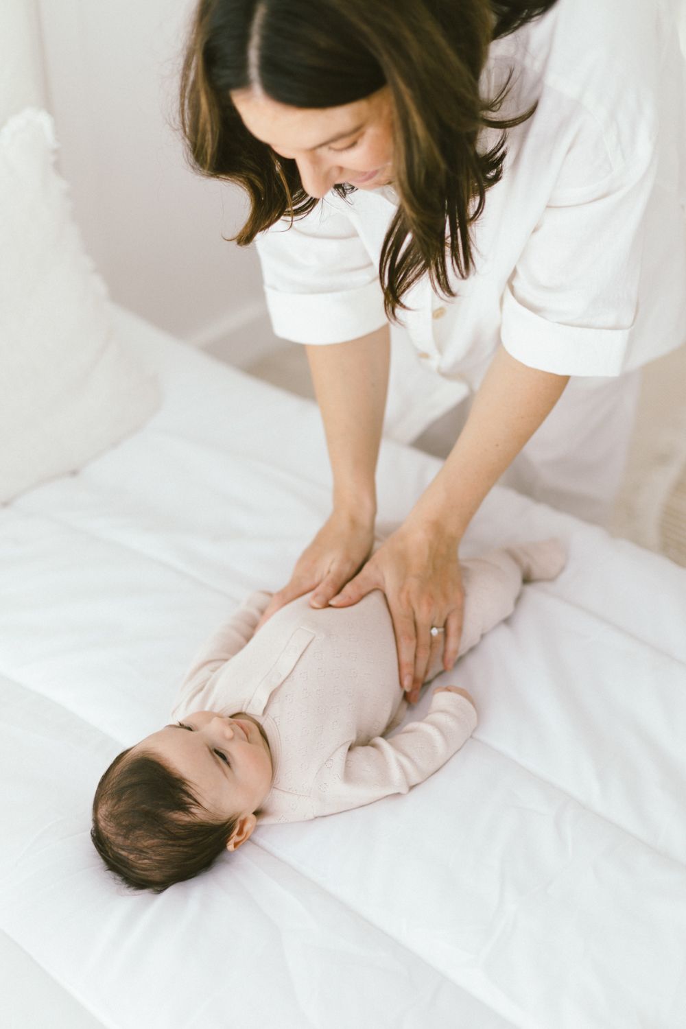 Caregiver in white shirt gently massaging infant on white bedding.