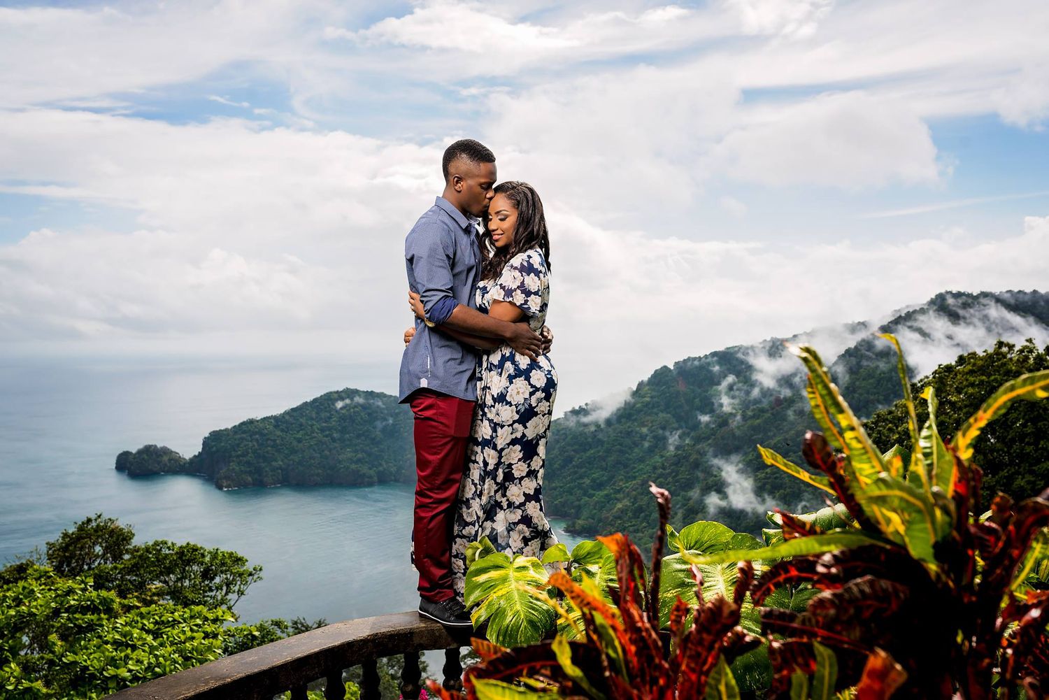 Couple shares intimate moment overlooking tropical mountain landscape.
