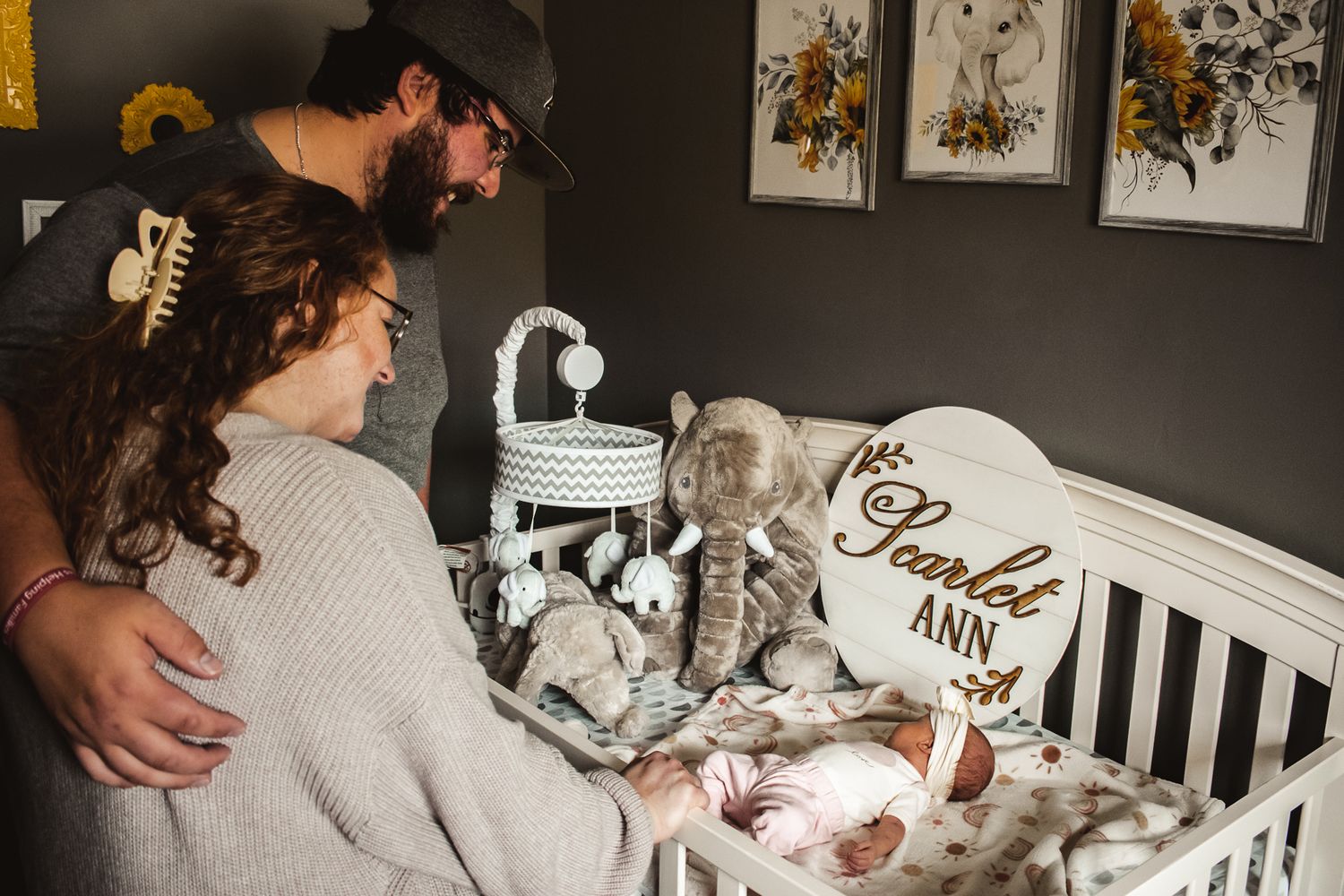 A cozy nursery scene with a white crib and floral artwork on dark walls.