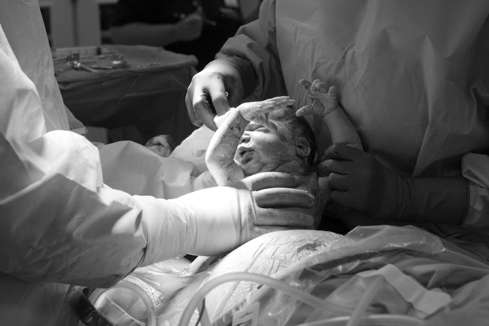 Medical staff perform examination on newborn baby in black and white hospital setting.