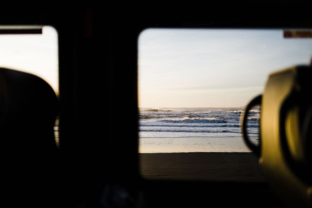 View of ocean waves through a vehicle window during golden hour sunset.