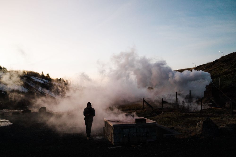 Silhouetted figure stands among rising steam in misty landscape.
