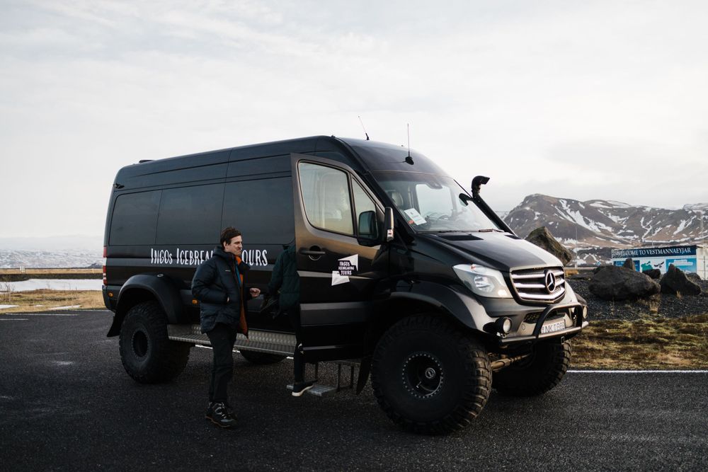 Black Mercedes-Benz off-road adventure van parked on mountain road with snowy peaks in background.