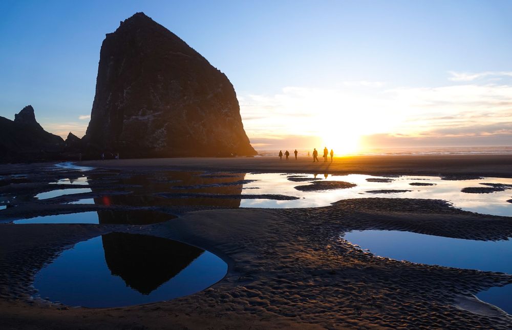 Dramatic sunset silhouettes Haystack Rock at Cannon Beach with tide pools reflecting golden light on the Oregon coast.