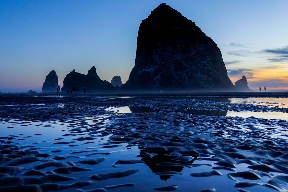 Haystack Rock and sea stacks create dramatic silhouettes against blue twilight reflections at Cannon Beach.