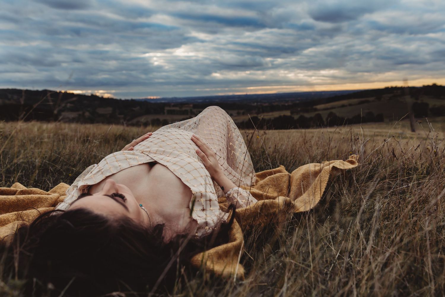 A pregnant woman, lying down in a field of grass with a sunset view
