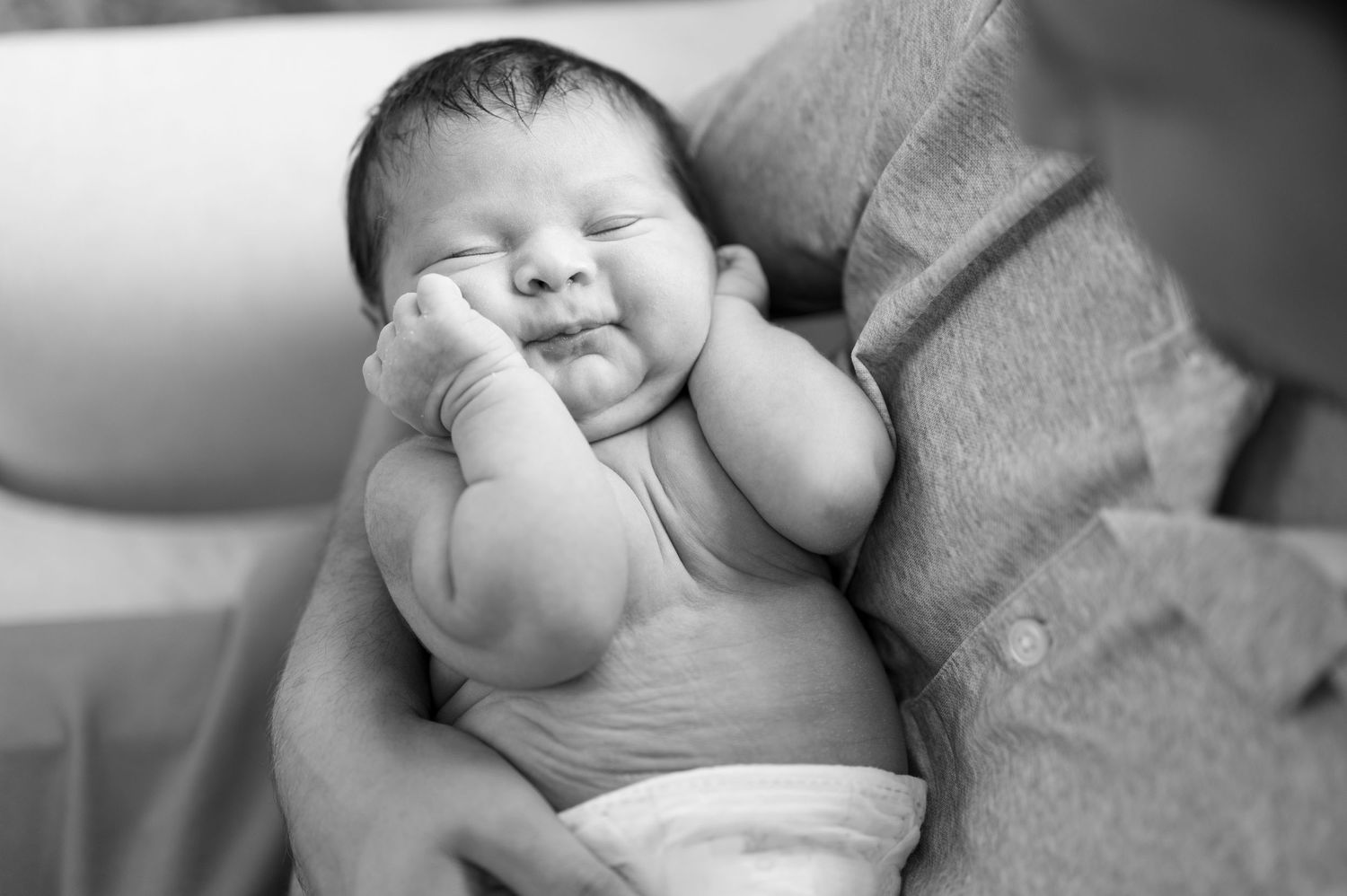 Black and white portrait of a chubby-cheeked newborn baby resting in father's arms.