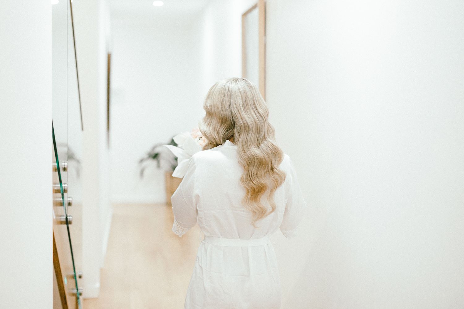 Back view of person with long blonde hair in white dress looking in mirror.