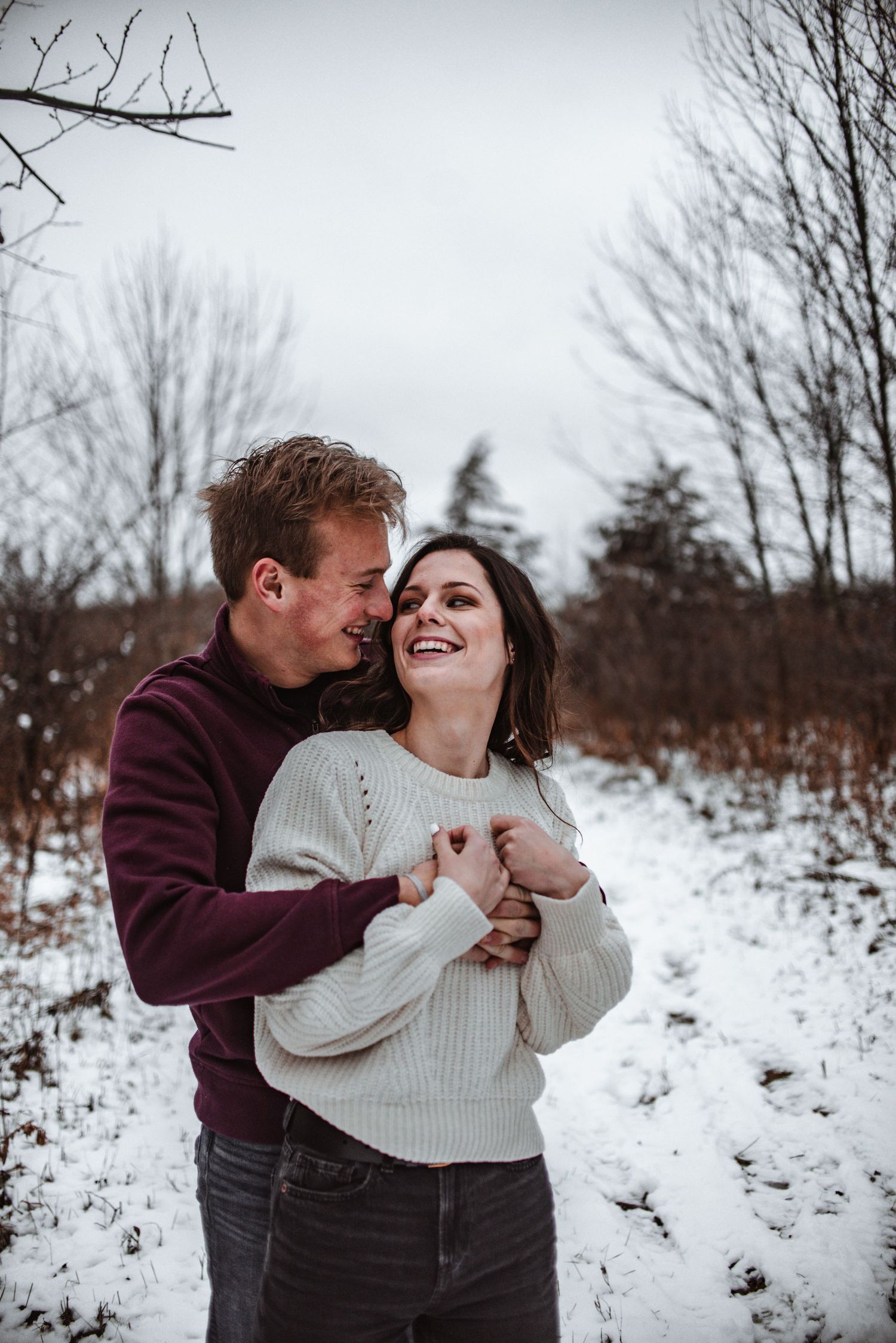 A playful winter engagement photo with a couple laughing in the snow.