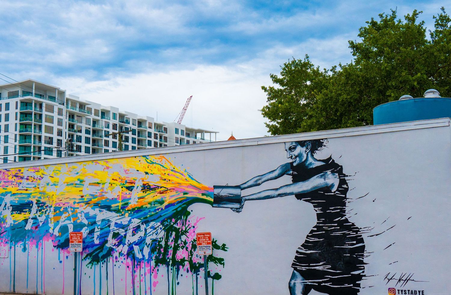 Colorful street art mural showing figure spraying rainbow colors on urban wall.