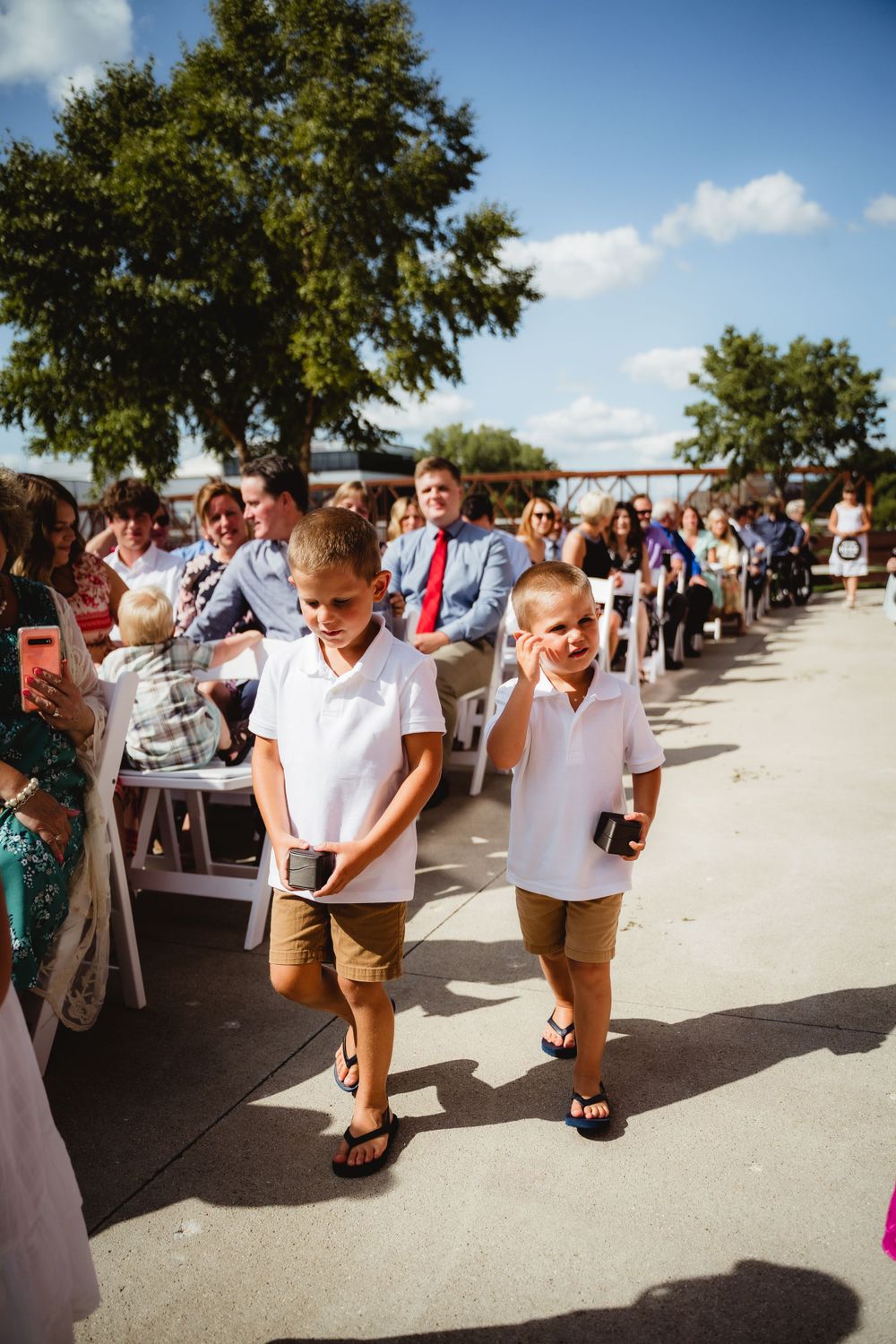 Two children walk down an outdoor ceremony pathway lined with white chairs.