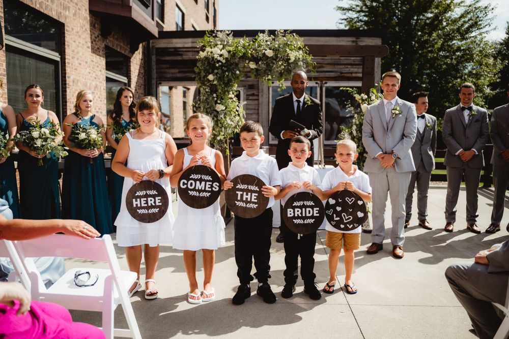 Group of children holding rustic wooden signs stand together at wedding ceremony.