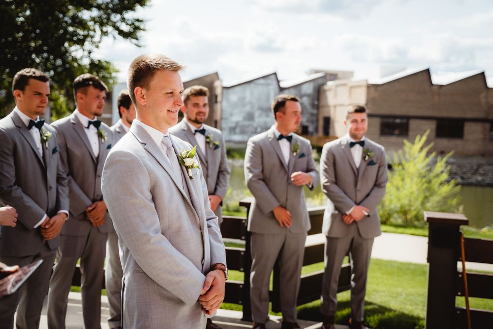 Groomsmen in gray suits stand in line during outdoor ceremony.
