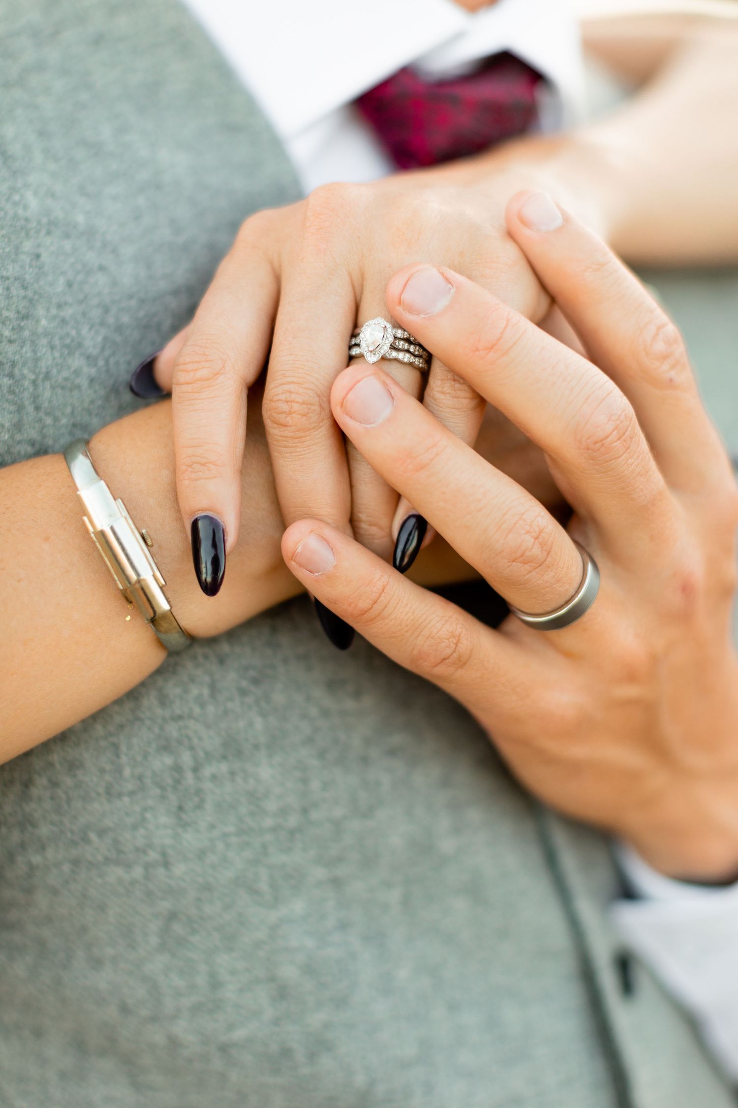 Close-up of intertwined hands showing wedding rings and elegant manicure.