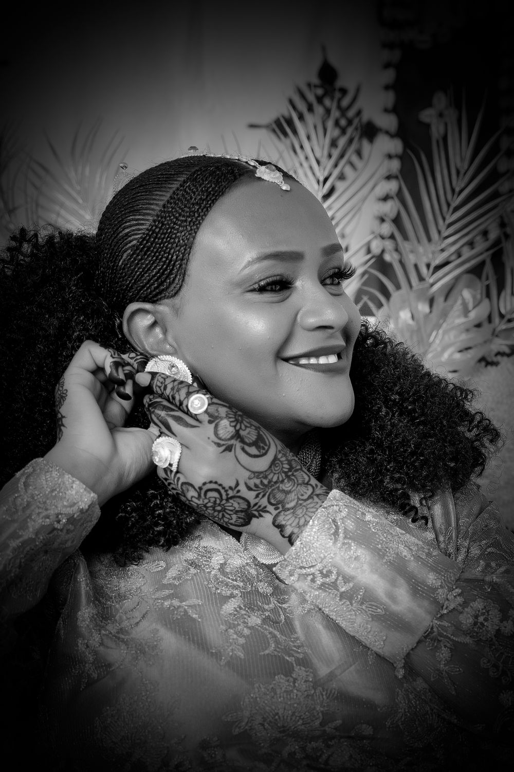 Black and white portrait showcasing intricate henna designs and traditional bridal jewelry against a patterned backdrop.