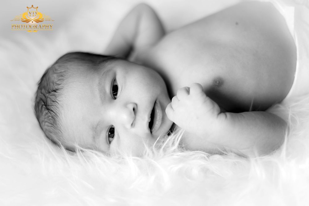 Black and white portrait of newborn baby lying on soft white fabric.