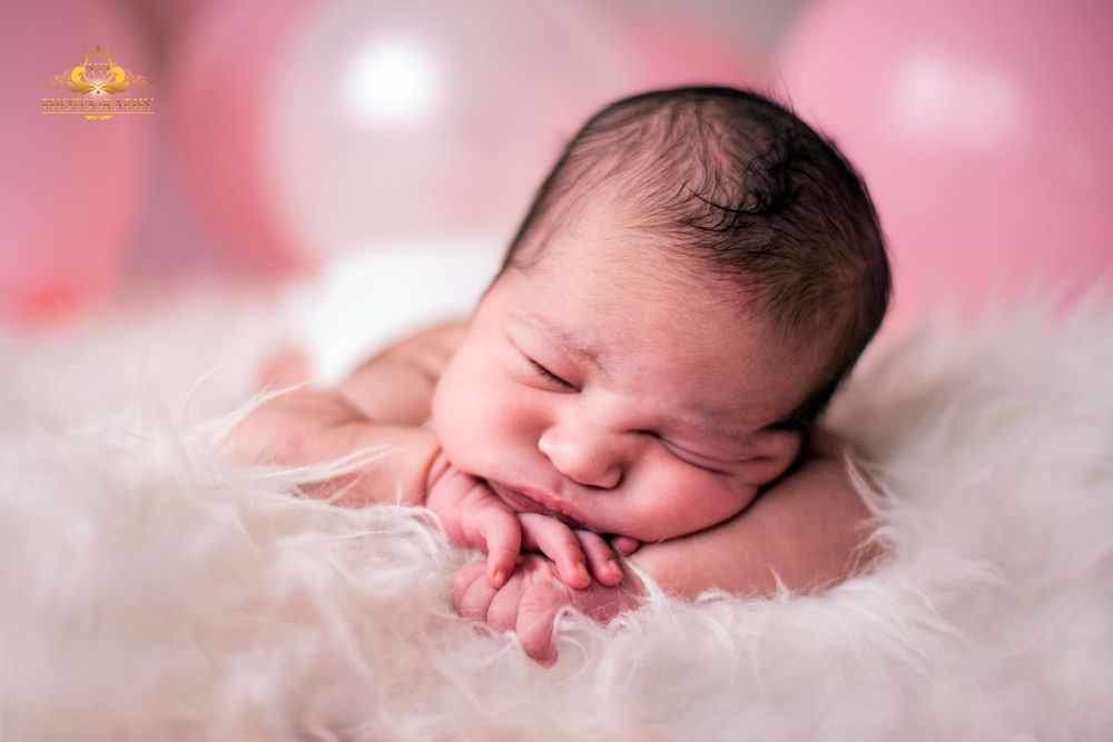 A sleeping newborn baby with hands tucked under chin on pink background.