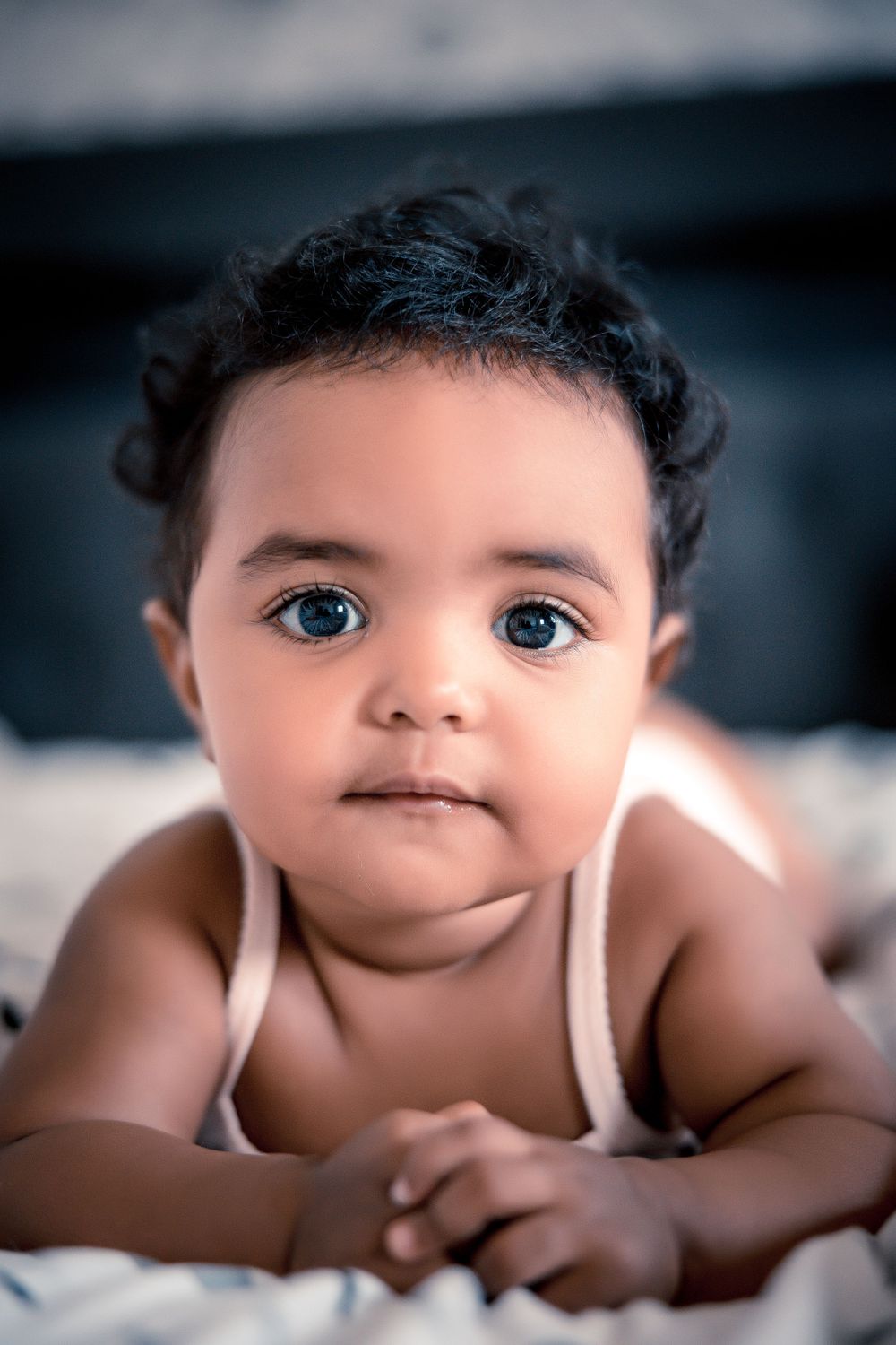 Close up of baby with curly hair and bright eyes laying on bedding.