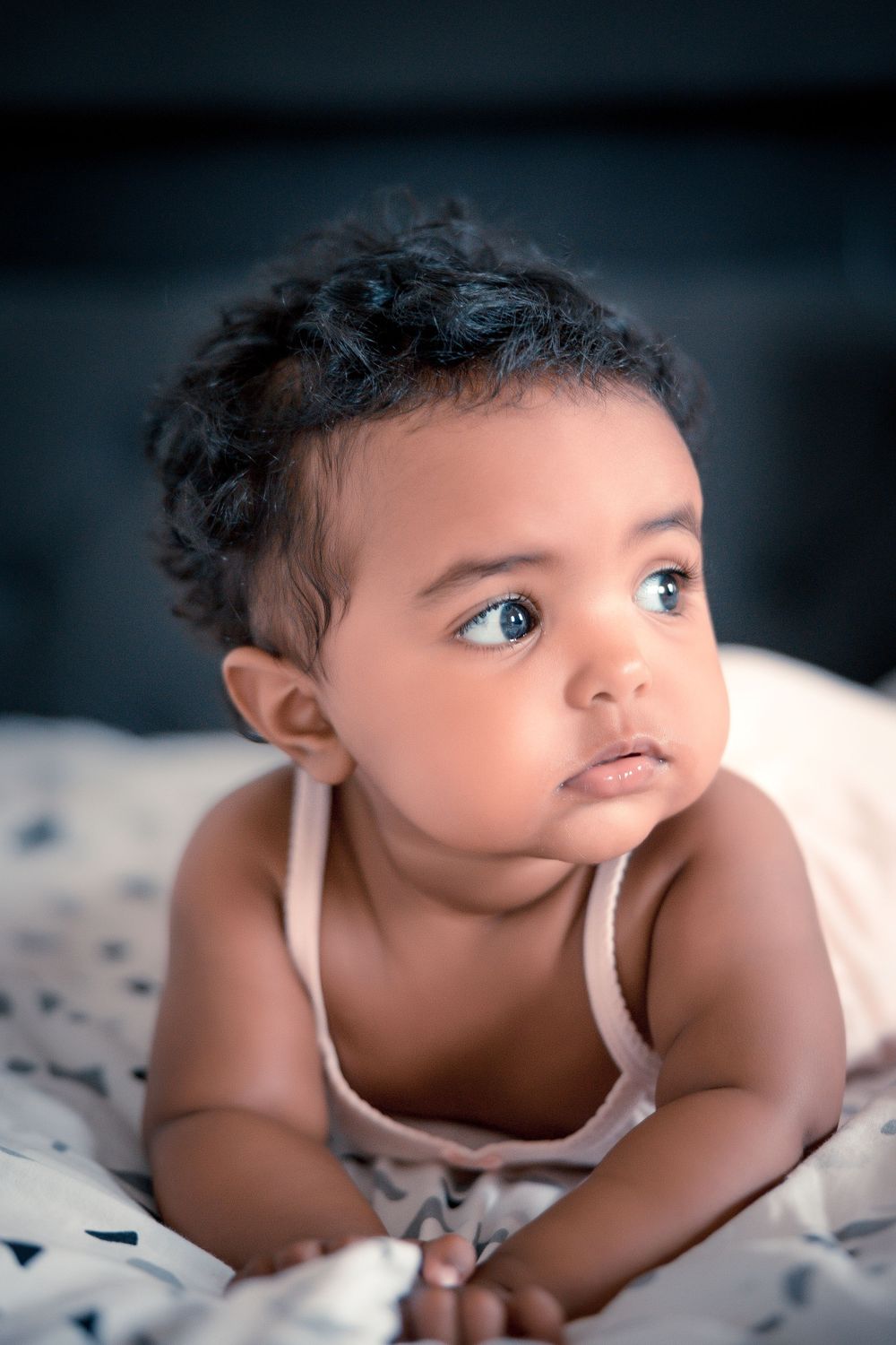 Close up portrait of baby in white tank top laying on patterned bedding.