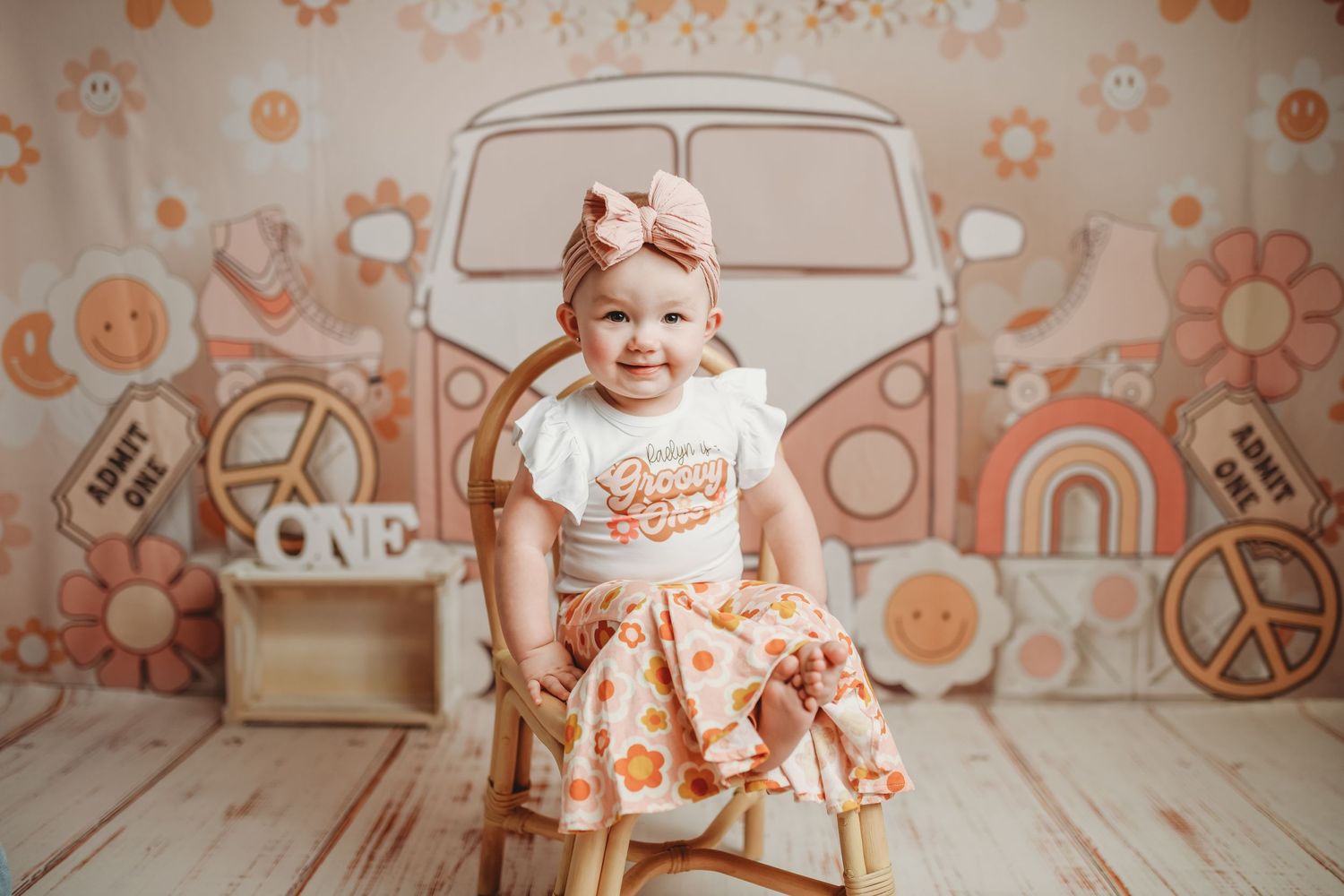 Toddler in peach dress poses against retro orange floral backdrop with VW bus illustration.