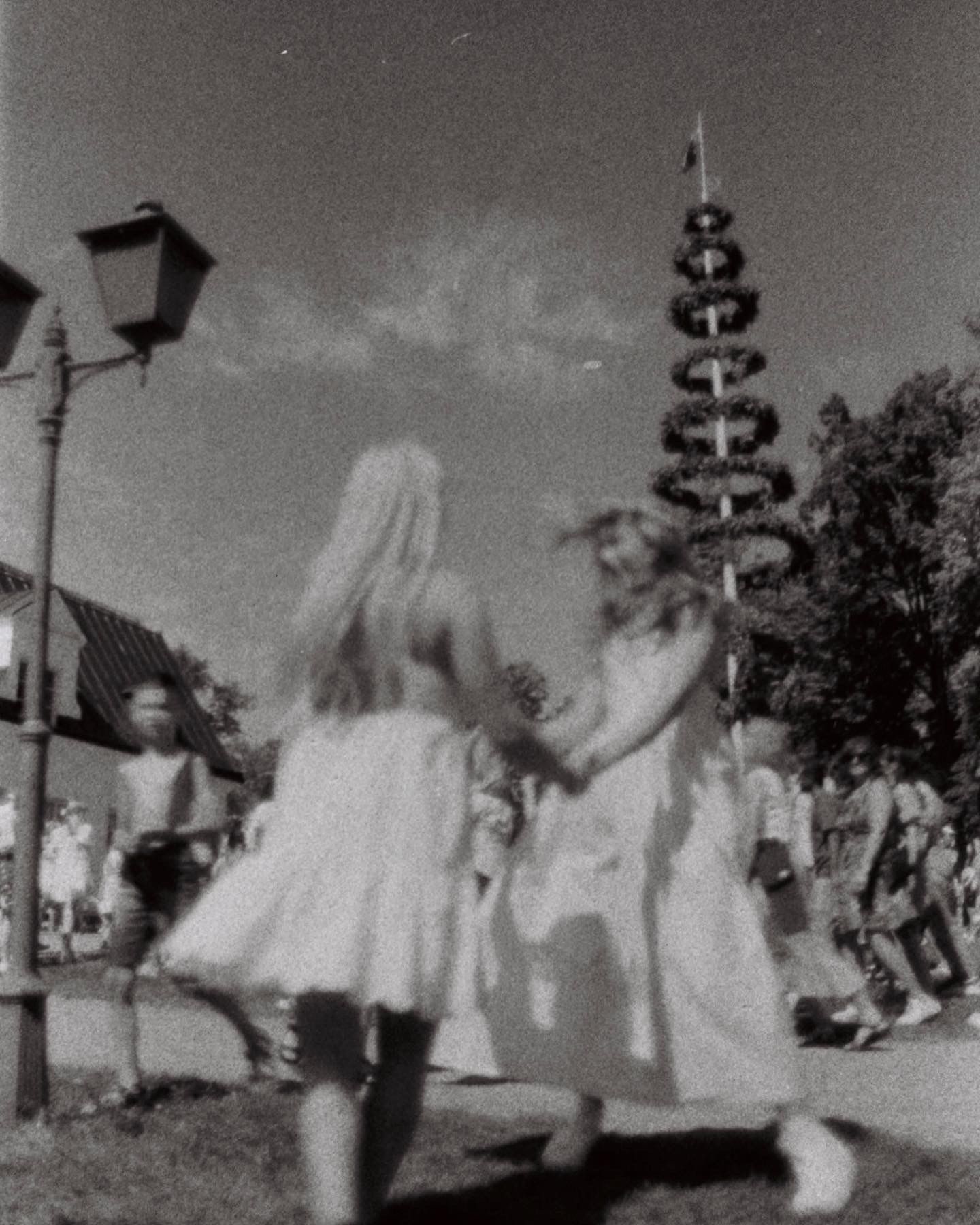 A black and white photo of children playing near a decorative street lamp and tower.
