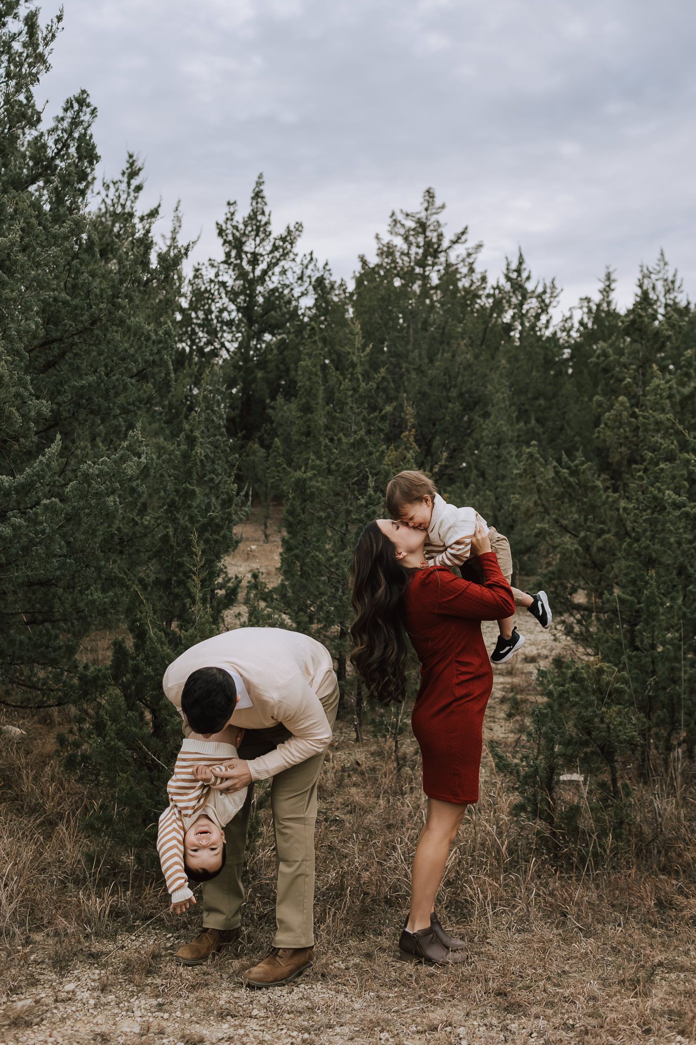 husband playing with son and mom playing wiht son infront of pine trees Family photographers kansas city