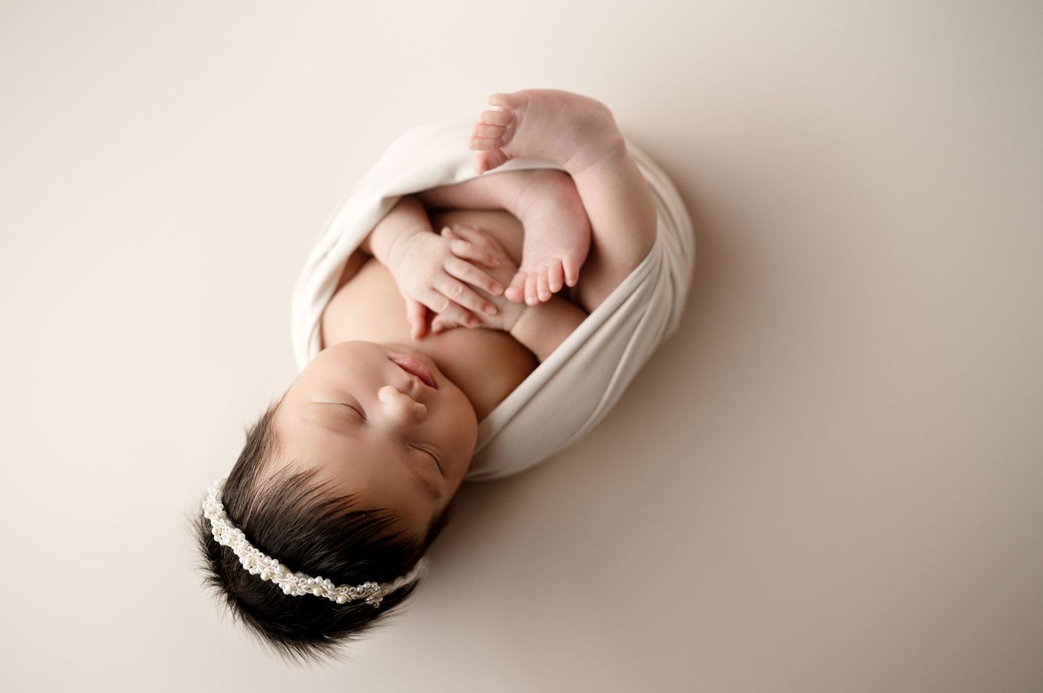 Simple portrait of sleeping newborn swaddled in white against soft beige backdrop.