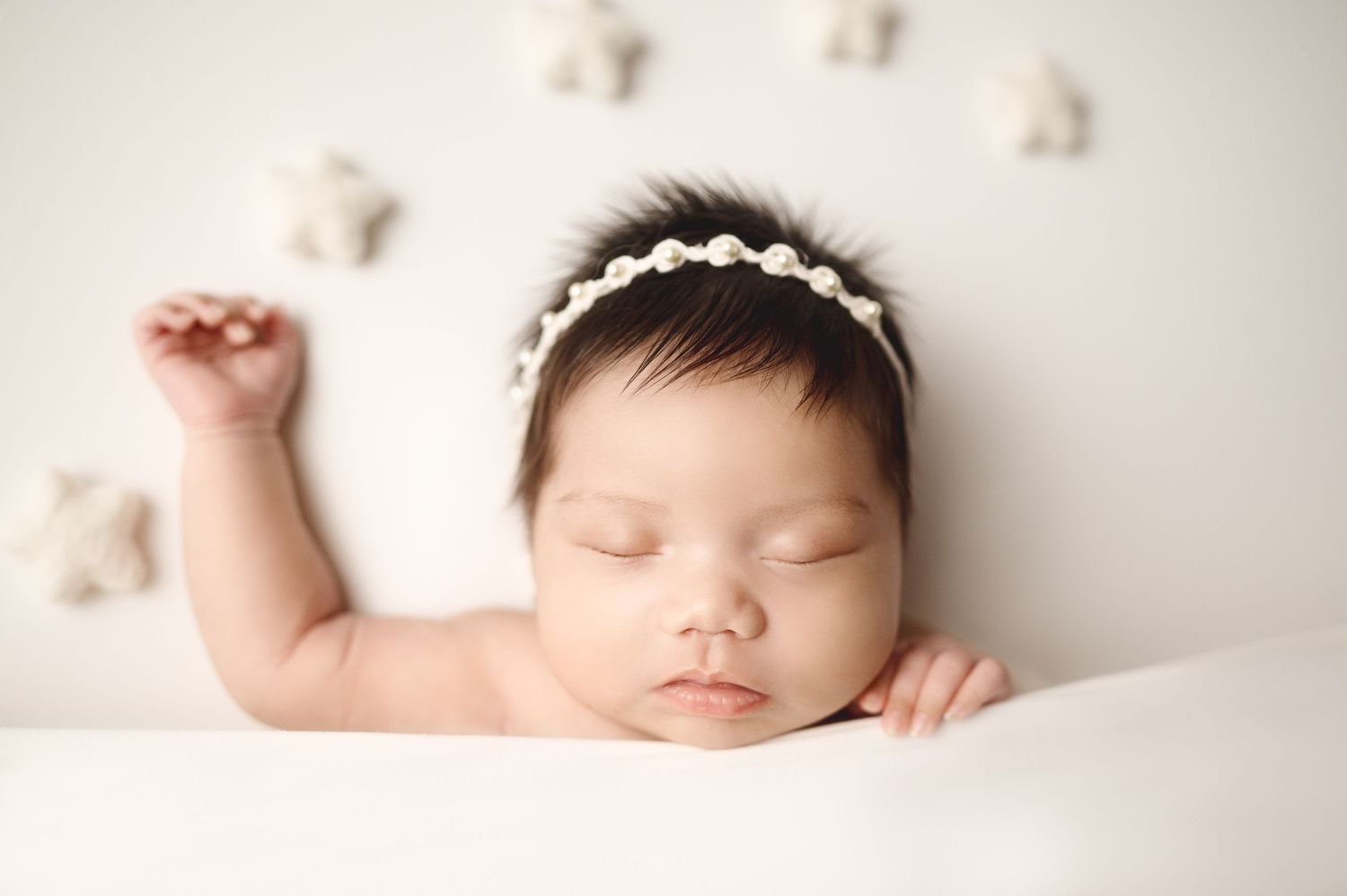 Sleeping newborn wearing lace headband with small decorative stars in background.
