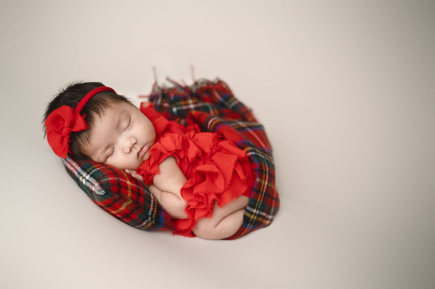Newborn baby sleeping peacefully in red and plaid holiday themed outfit.