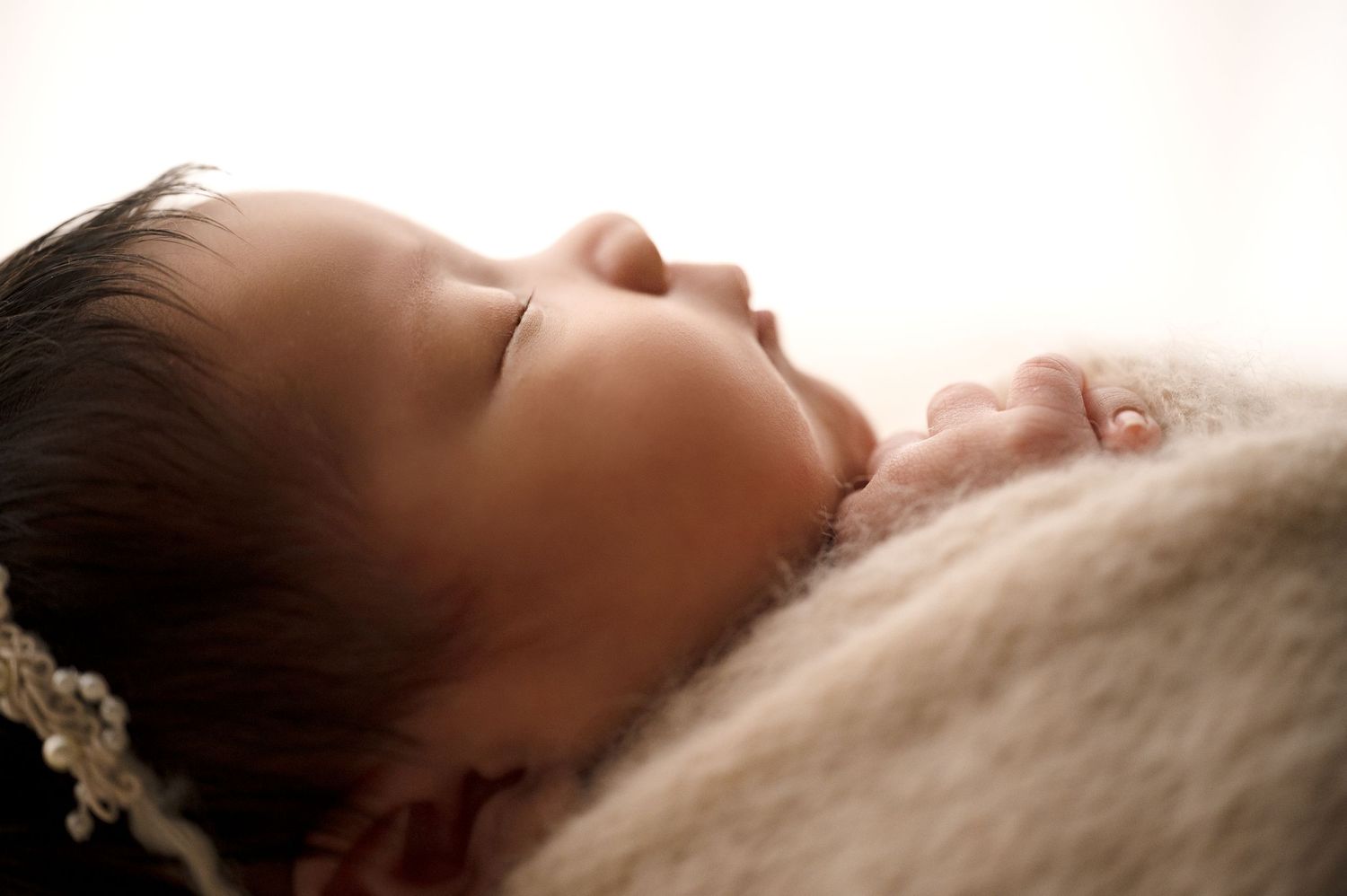 Side profile of sleeping newborn on soft textured blanket in warm tones.