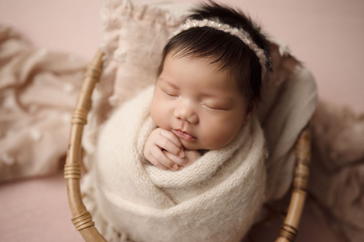 Newborn baby sleeping soundly in cream colored swaddle wrap.