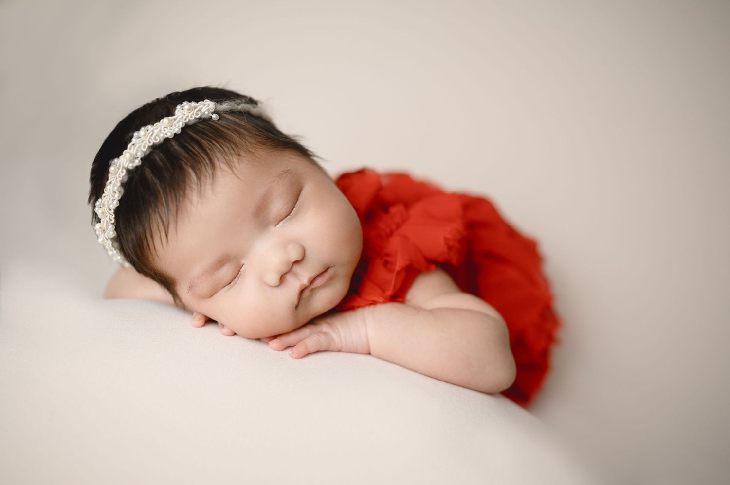 Sleeping newborn portrait series with red accessories on neutral background.