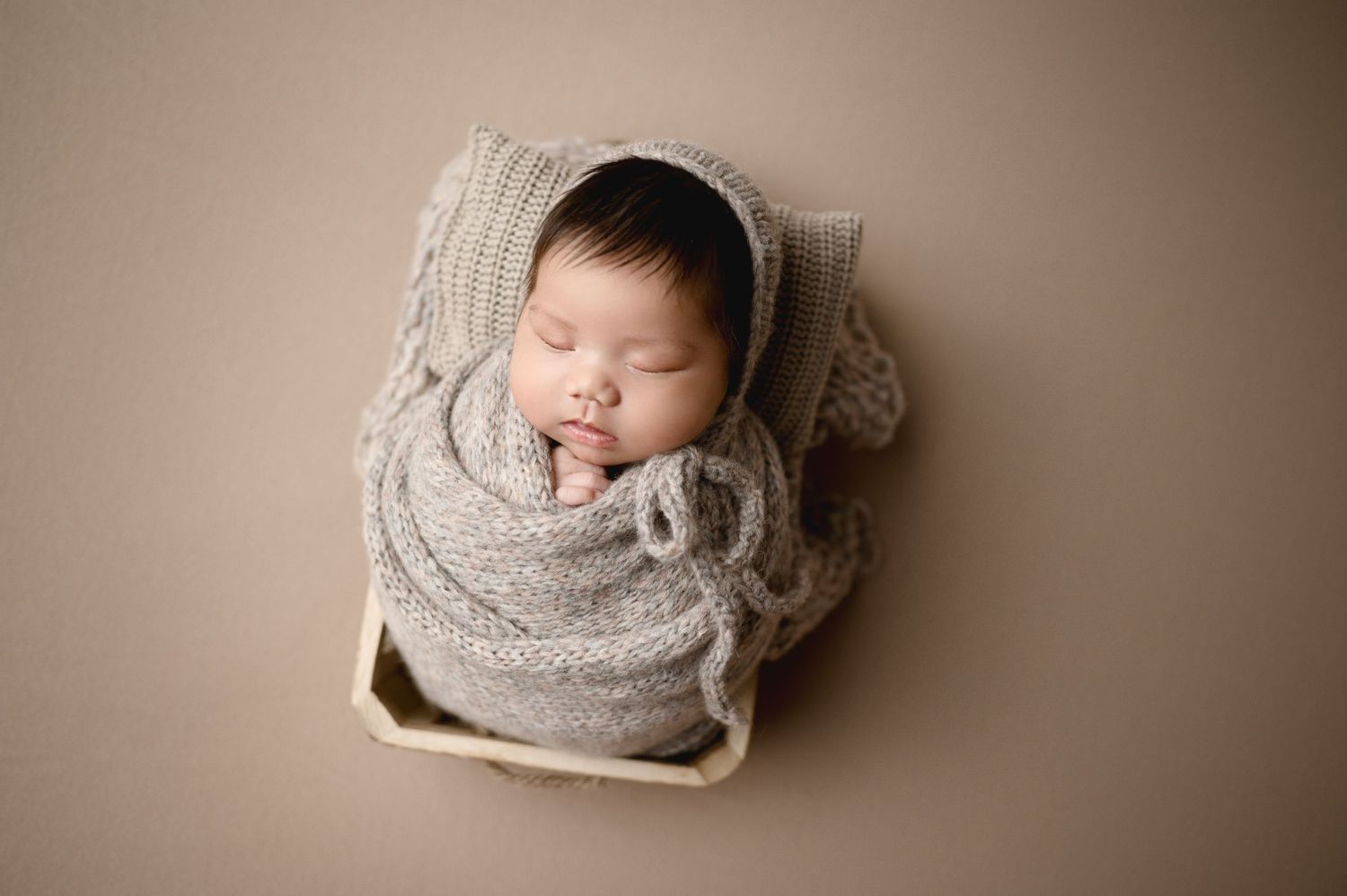 Collection of artistic newborn portraits with gray knit wrap on beige backdrop.