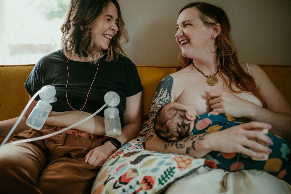 queer & trans parents laugh with each other during co feeding session in home newborn photography portland oregon