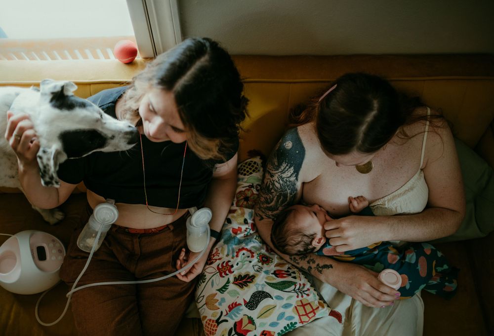 queer parent pumps breastmilk while trans parent uses SNS to feed baby in home baby session portland oregon