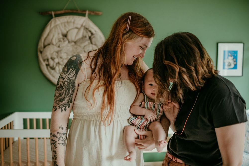trans queer parents hold baby in home baby photography session portland oregon